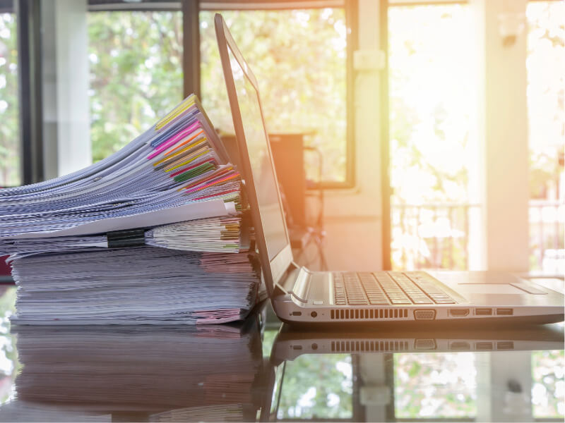 Stack of papers next to a laptop