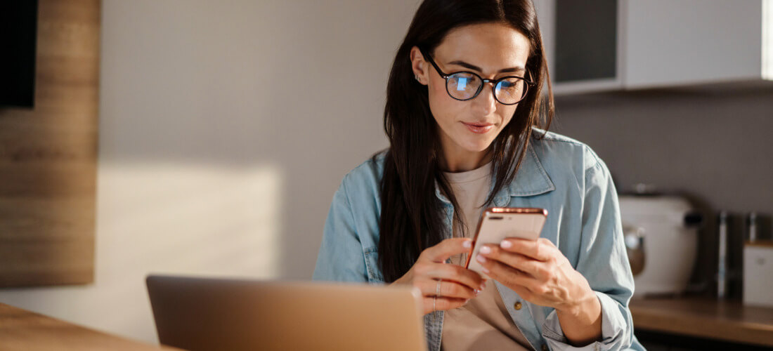 Woman using smartphone while working with laptop